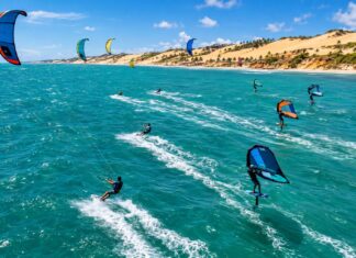 Kitesurf e wingfoil no Ceará: o vento que move R$ 1,66 bilhão e ainda espera por regras Aerial action photo of kitesurfers and wingfoil riders racing across turquoise ocean water with strong wind-filled kites…