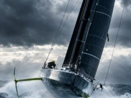 Editorial photography of a high-performance IMOCA 60 offshore racing sailboat with hydrofoils, heeling and flying across…