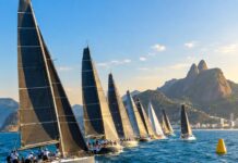 Refeno 2026: recorde de embarcações larga em busca de destronar o Adrenalina Pura Fleet of racing sailboats at the starting line of an offshore ocean regatta, dramatic wide shot, blue tropical ocean, cl…