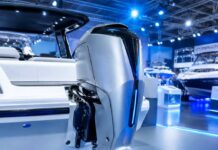 Fotografia realista de um motor de popa moderno e futurista instalado na traseira de uma lancha branca, em um salão náut…