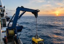 Fotografia realista de um navio de pesquisa oceanográfica no meio do Oceano Atlântico, em alto-mar, com um ROV (veículo …