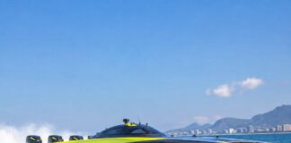 Uma lancha catamarã de competição offshore em altíssima velocidade, cortando as águas do litoral brasileiro em pleno dia…