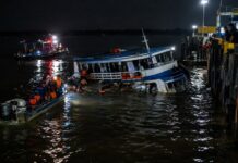 A small passenger ferry boat partially sunk at night near a river port dock in the Amazon region of northern Brazil, dar…