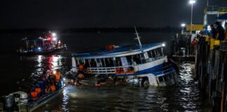 A small passenger ferry boat partially sunk at night near a river port dock in the Amazon region of northern Brazil, dar…