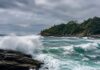 Naufrágio em Ilhabela expõe falhas de segurança no mar Foto realista de um mar agitado batendo em rochas na costa de uma ilha tropical brasileira, céu nublado, sem pessoas, se…