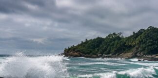 Foto realista de um mar agitado batendo em rochas na costa de uma ilha tropical brasileira, céu nublado, sem pessoas, se…