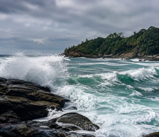 Foto realista de um mar agitado batendo em rochas na costa de uma ilha tropical brasileira, céu nublado, sem pessoas, se…